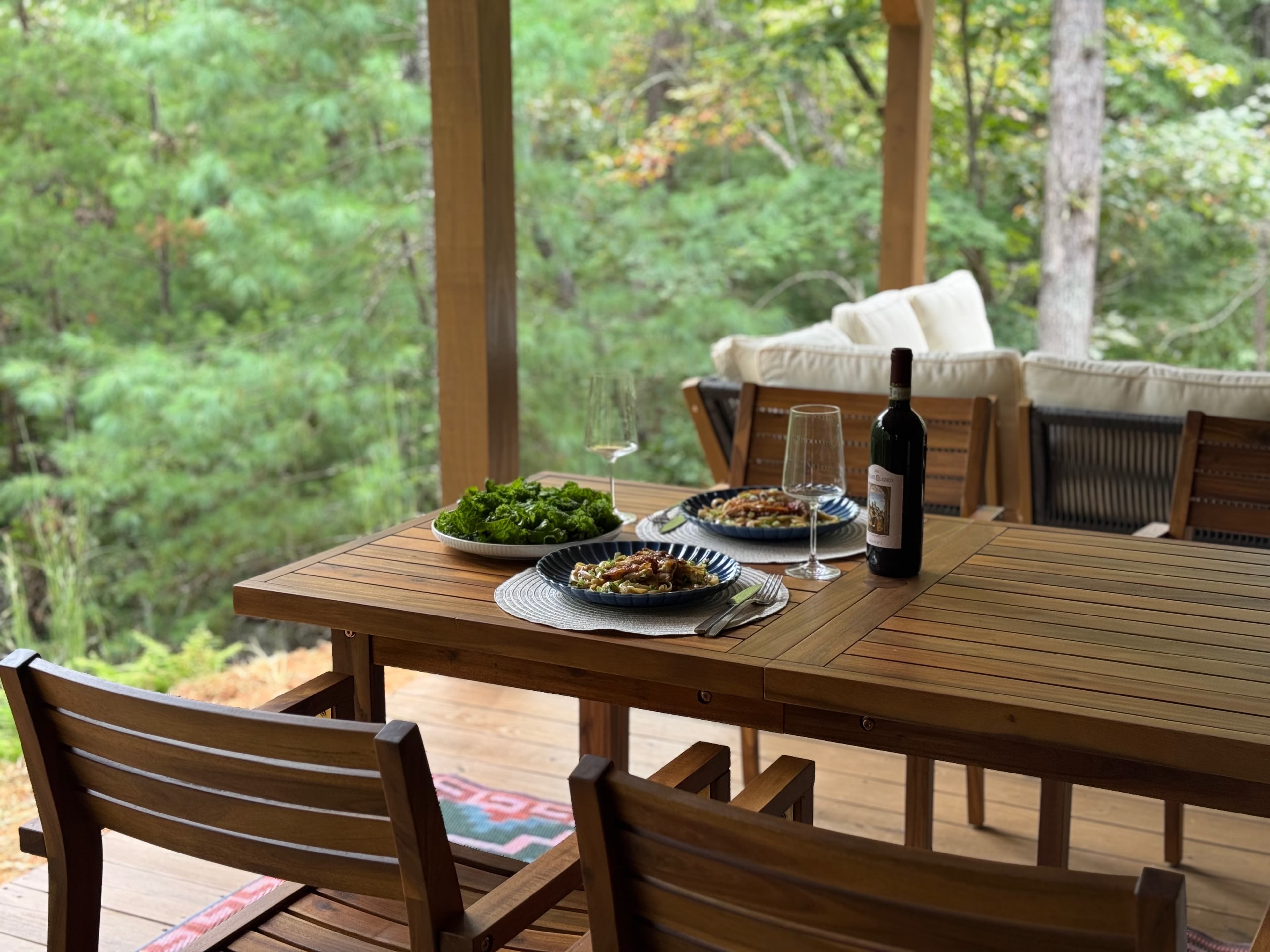 Dinner and wine set out on the deck table, forest just beyond the railing