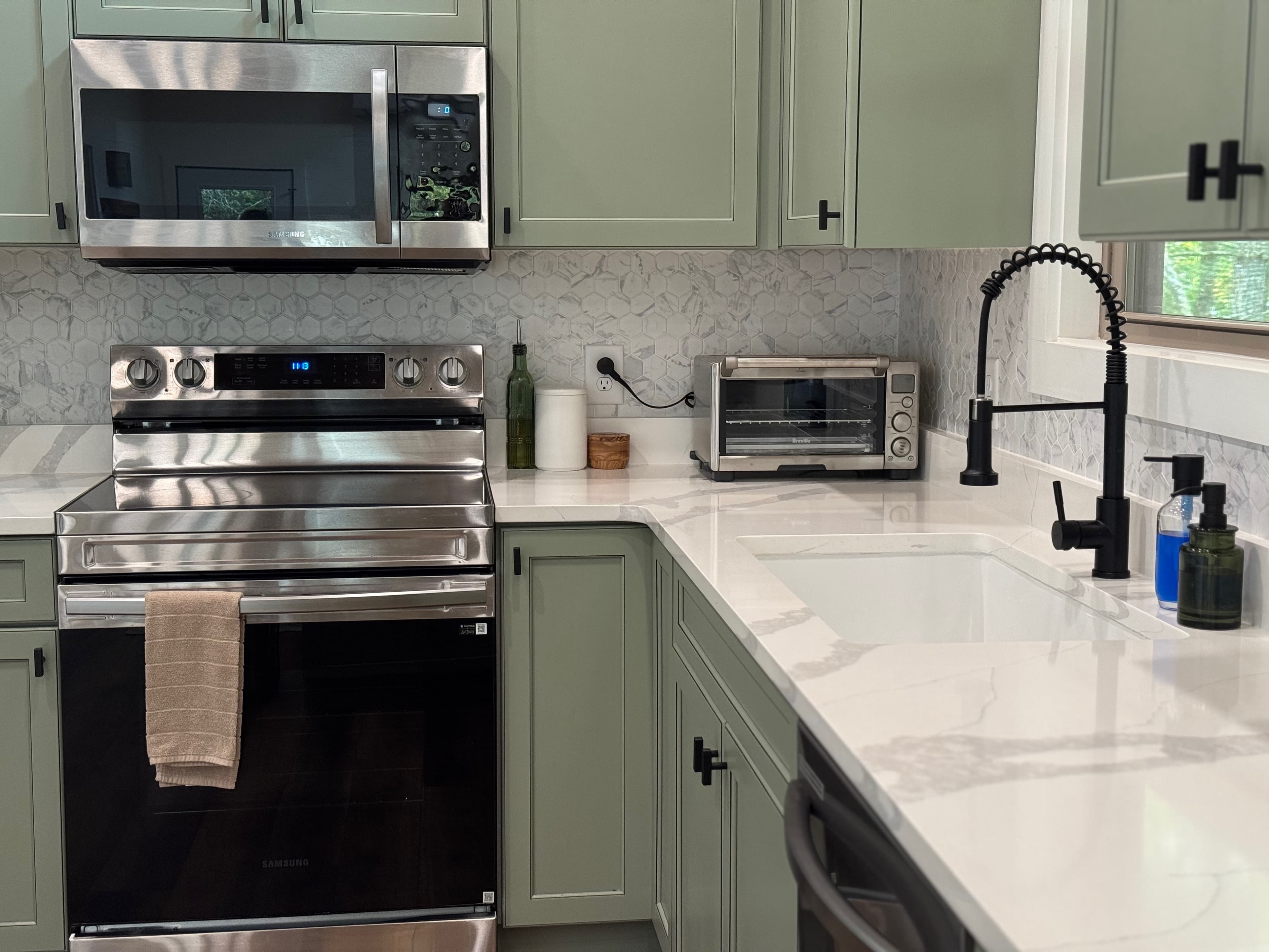 Fully stocked kitchen with sage cabinets, marble backsplash, and stainless appliances