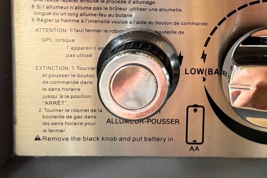 Fire pit igniter button next to the spare AA battery and instructions